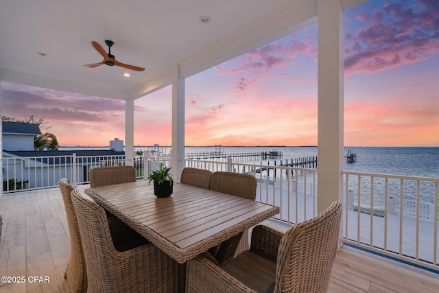 wooden deck featuring a water view, outdoor dining area, and a ceiling fan