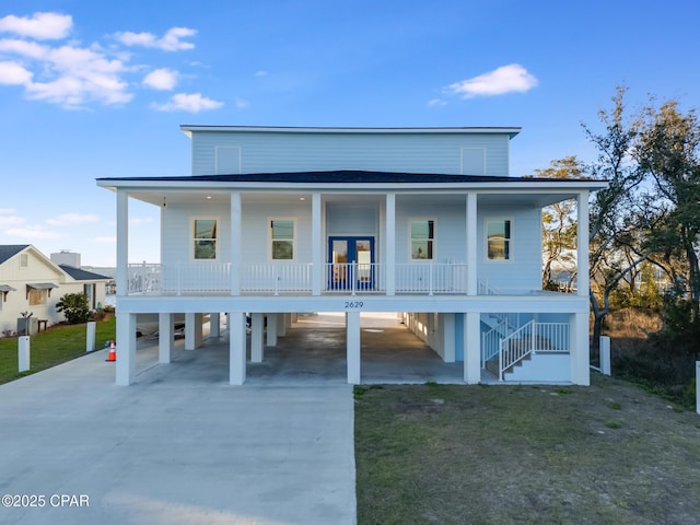 coastal inspired home featuring driveway, stairway, french doors, a porch, and a carport