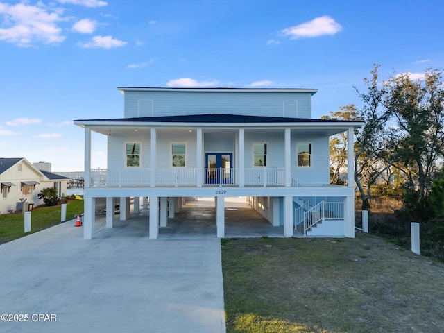 raised beach house with concrete driveway, stairway, a porch, a carport, and a front yard