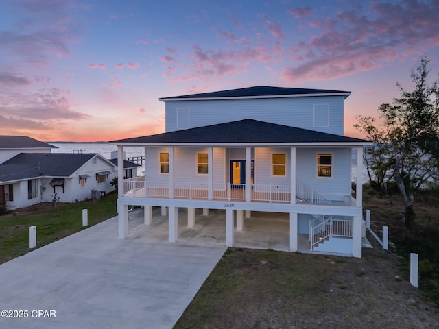 view of front of property with a yard, a shingled roof, covered porch, concrete driveway, and stairs