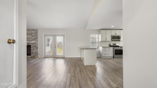 unfurnished living room featuring light wood-style floors, baseboards, a stone fireplace, and french doors