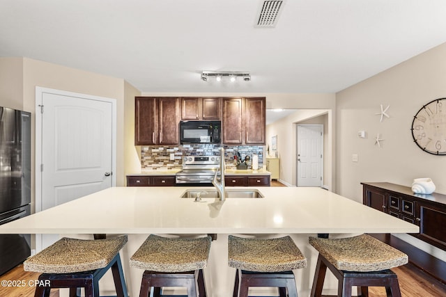 kitchen with a sink, light countertops, black appliances, tasteful backsplash, and a center island with sink