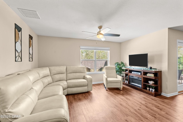 living area with ceiling fan, light wood-type flooring, visible vents, and baseboards