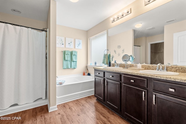 bathroom with a garden tub, double vanity, visible vents, a sink, and wood finished floors