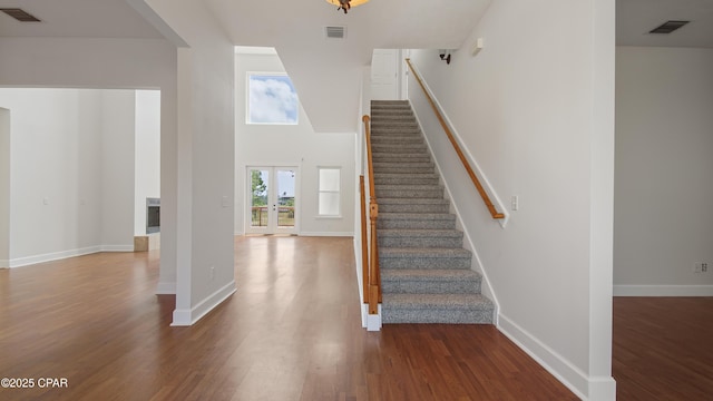 stairs featuring a towering ceiling, french doors, wood finished floors, and visible vents