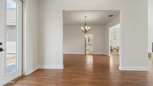 spare room featuring a chandelier, wood finished floors, visible vents, and baseboards