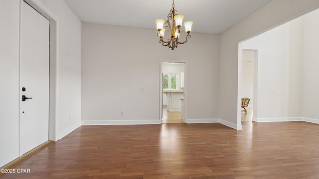 unfurnished room with baseboards, wood finished floors, and an inviting chandelier