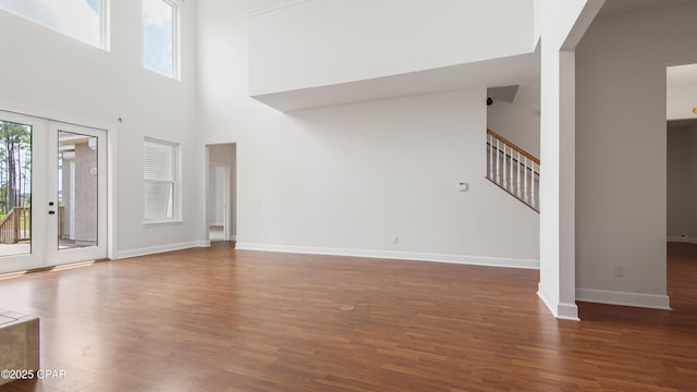 unfurnished living room with a high ceiling, wood finished floors, baseboards, stairs, and french doors