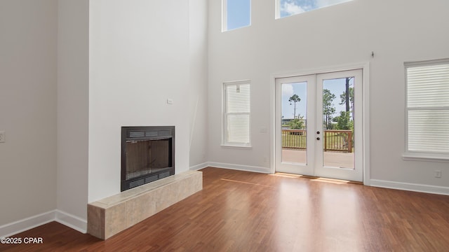 unfurnished living room featuring a tile fireplace, dark wood-style flooring, a towering ceiling, baseboards, and french doors