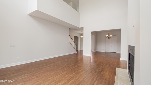 unfurnished living room featuring baseboards, a fireplace with flush hearth, wood finished floors, stairs, and a notable chandelier