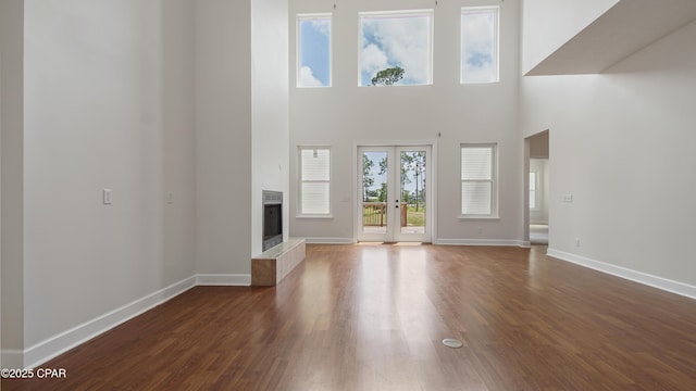 unfurnished living room featuring a fireplace, a towering ceiling, baseboards, french doors, and dark wood finished floors