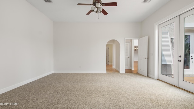 carpeted empty room with baseboards, visible vents, arched walkways, a ceiling fan, and french doors