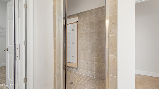 full bath featuring a spacious closet, a stall shower, and baseboards