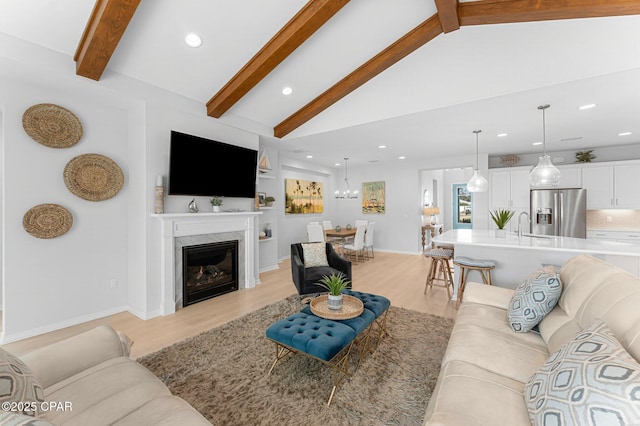 living room featuring lofted ceiling with beams, light wood finished floors, recessed lighting, and a glass covered fireplace