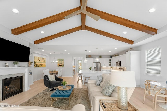 living area featuring lofted ceiling with beams, a glass covered fireplace, light wood-style flooring, and recessed lighting