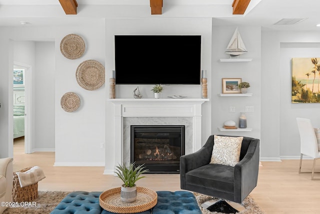 living area featuring visible vents, a premium fireplace, light wood-type flooring, and beam ceiling