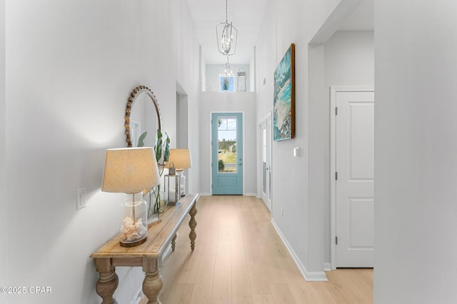 entryway with light wood finished floors, baseboards, and a notable chandelier