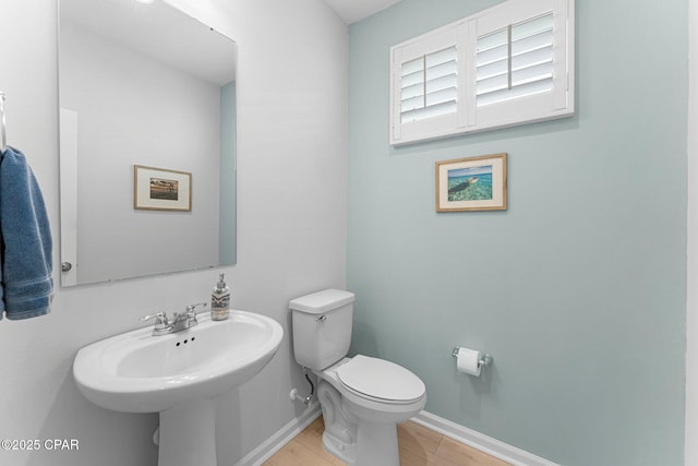 half bathroom featuring baseboards, a sink, toilet, and wood finished floors