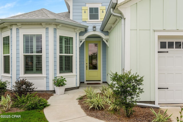 view of exterior entry with a garage, a shingled roof, and board and batten siding