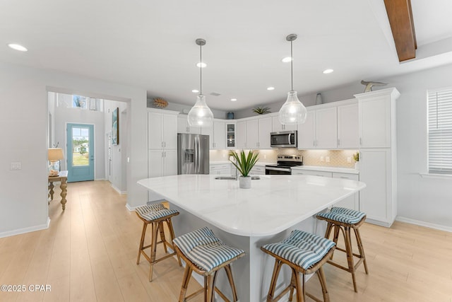 kitchen with light wood-style flooring, a kitchen breakfast bar, white cabinets, appliances with stainless steel finishes, and tasteful backsplash