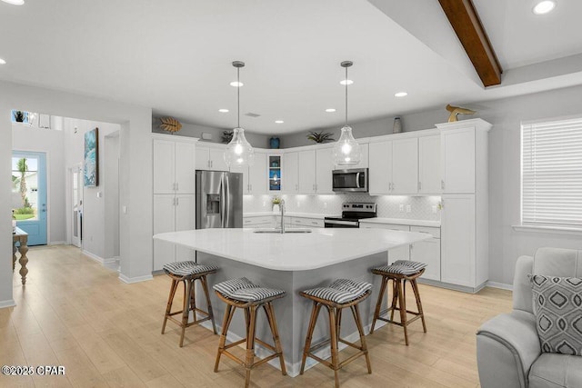 kitchen with a sink, light wood-style floors, white cabinets, appliances with stainless steel finishes, and tasteful backsplash