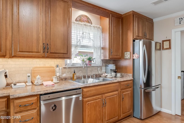 kitchen with brown cabinets, crown molding, decorative backsplash, appliances with stainless steel finishes, and a sink