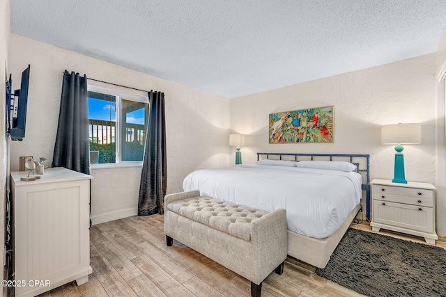 bedroom featuring baseboards, a textured wall, light wood-style flooring, and a textured ceiling