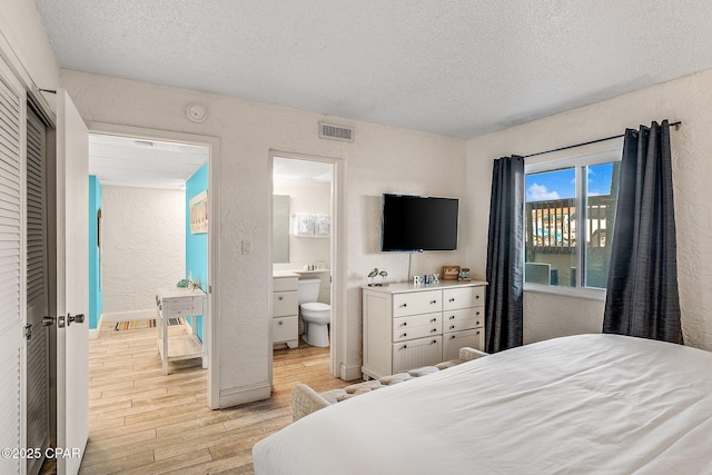 bedroom with visible vents, a textured wall, light wood-style flooring, ensuite bathroom, and a textured ceiling