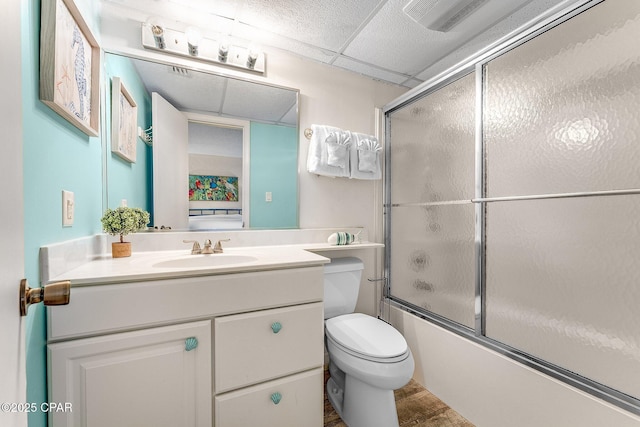 full bathroom featuring visible vents, toilet, combined bath / shower with glass door, vanity, and a drop ceiling