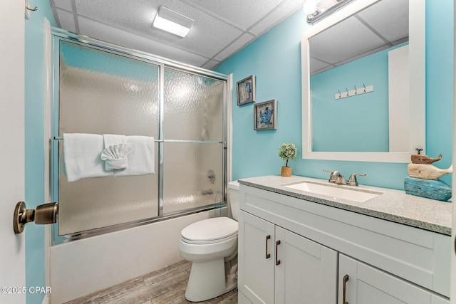 full bath featuring bath / shower combo with glass door, toilet, vanity, wood finished floors, and a drop ceiling