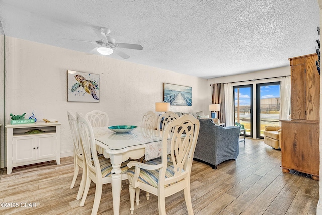 dining space featuring a textured ceiling, a textured wall, light wood finished floors, and a ceiling fan