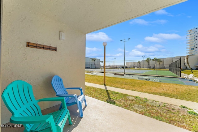 view of patio with a tennis court and fence