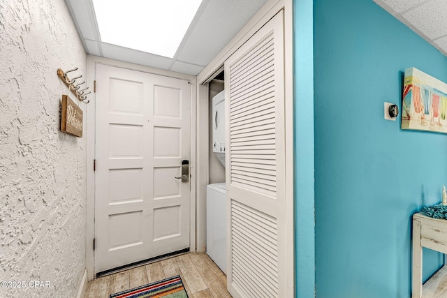 interior space with a paneled ceiling, light wood-style floors, stacked washer / dryer, and a textured wall