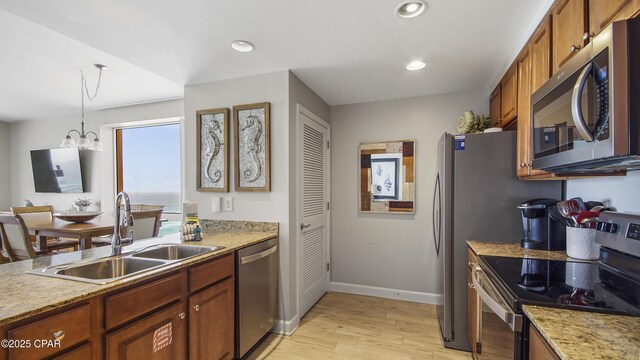 kitchen featuring appliances with stainless steel finishes, brown cabinetry, a sink, and an inviting chandelier