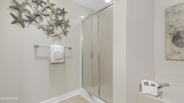 full bath featuring a stall shower, wood finished floors, a bath, and baseboards