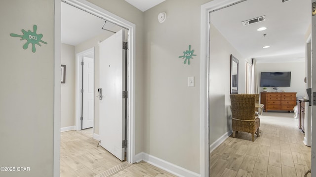 hallway featuring baseboards, visible vents, and light wood finished floors