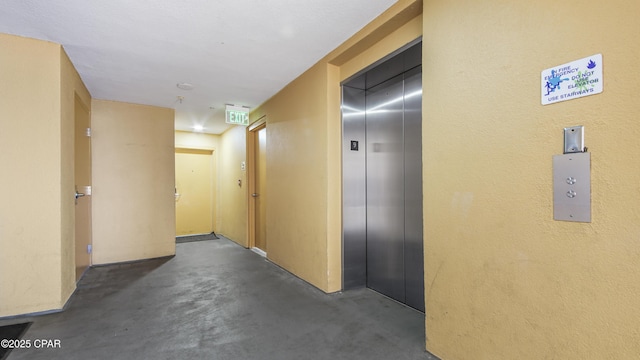 hallway with elevator and concrete flooring
