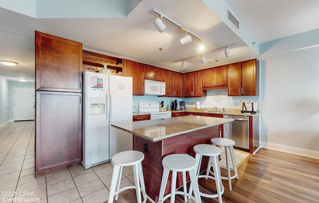 kitchen with a center island, visible vents, a sink, white appliances, and a kitchen breakfast bar