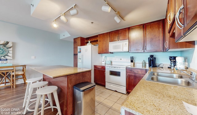 kitchen featuring white appliances, a kitchen island, a kitchen breakfast bar, light countertops, and a sink