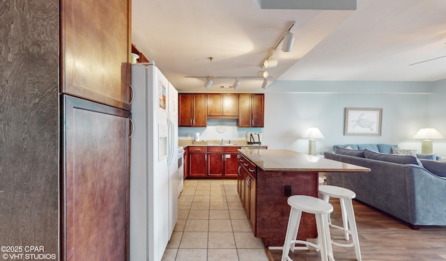 kitchen featuring a center island, light countertops, open floor plan, white appliances, and a kitchen bar