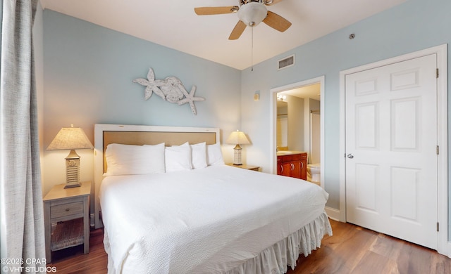 bedroom featuring ensuite bathroom, wood finished floors, visible vents, and a ceiling fan