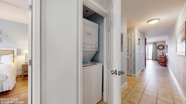 washroom with light tile patterned floors, laundry area, stacked washer and clothes dryer, and baseboards