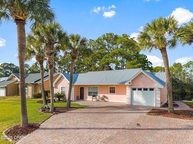 ranch-style home featuring metal roof, a garage, decorative driveway, stucco siding, and a front yard