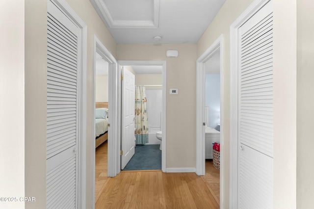 corridor with light wood-style floors, attic access, and baseboards