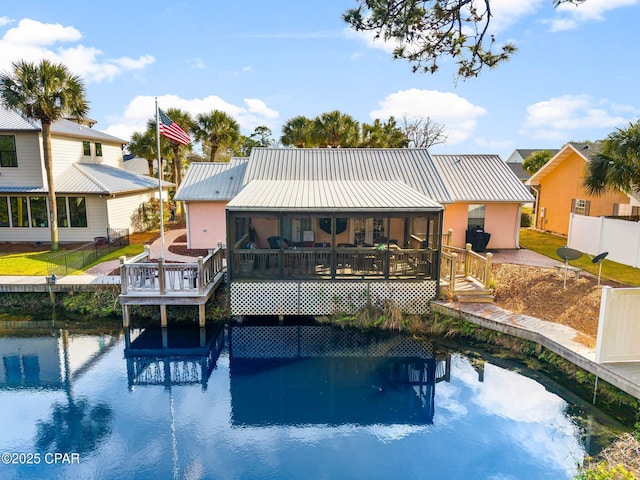 back of house with metal roof, a deck with water view, fence, and stucco siding