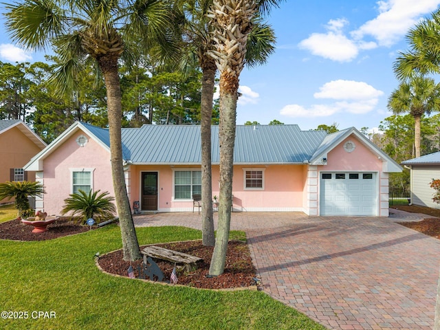 ranch-style home with metal roof, a garage, decorative driveway, stucco siding, and a front lawn