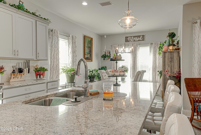 kitchen featuring light stone counters, backsplash, a sink, and a kitchen breakfast bar