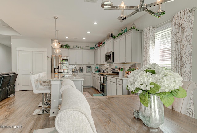 kitchen with light wood finished floors, a kitchen island with sink, stainless steel appliances, and decorative backsplash