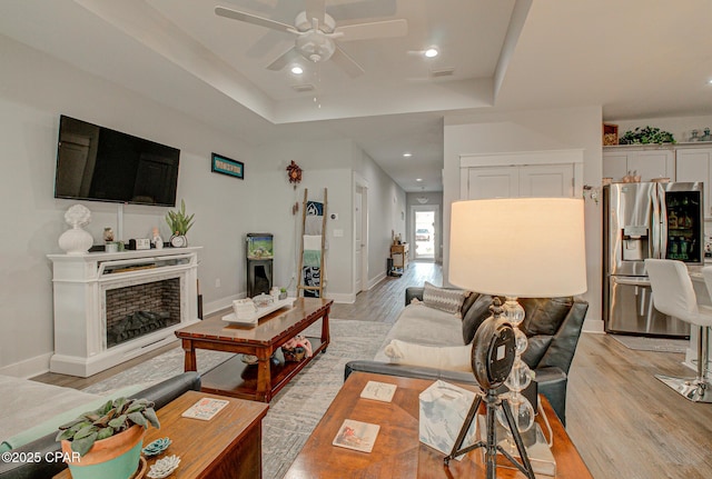 living area with light wood-style floors, a raised ceiling, a fireplace, and baseboards