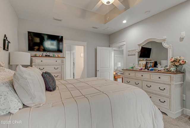 bedroom featuring ceiling fan, visible vents, a tray ceiling, and light colored carpet